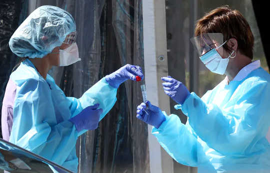 Medical personnel secure a sample from a person at a drive-through coronavirus COVID-19 testing station