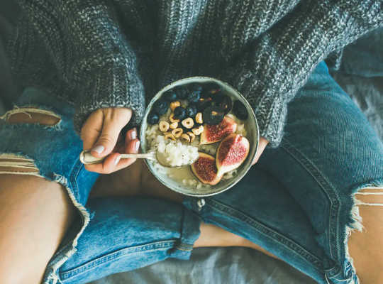 Woman holds healthy breakfast bowl with blueberries, guava and cereal.