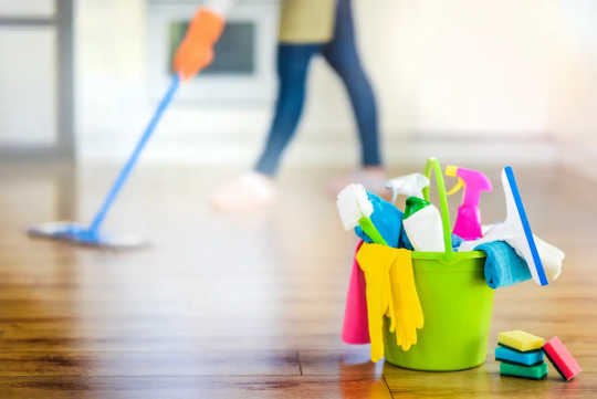 A colourful bucket of cleaning products, with a woman mopping in the background.
