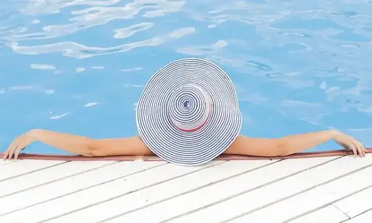 Women laying in the pool with her arms on the edge, wearing a sun hat