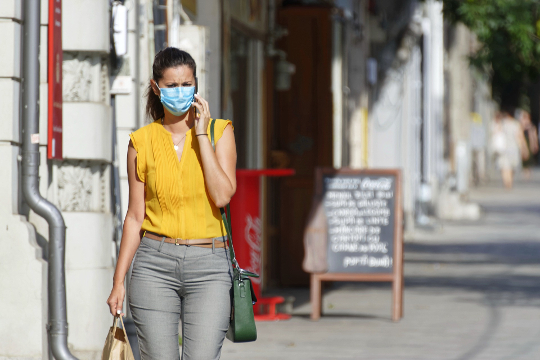 woman walking down the street wearing a mask and touching her face