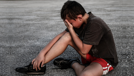 boy sitting on the pavement holding his ankle and his head... seemingly in pain