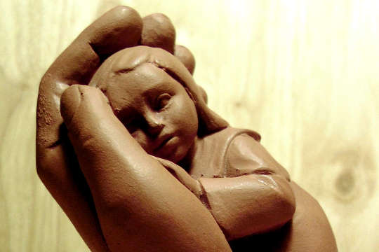 a clay sculpture of a child being held in a supportive hand