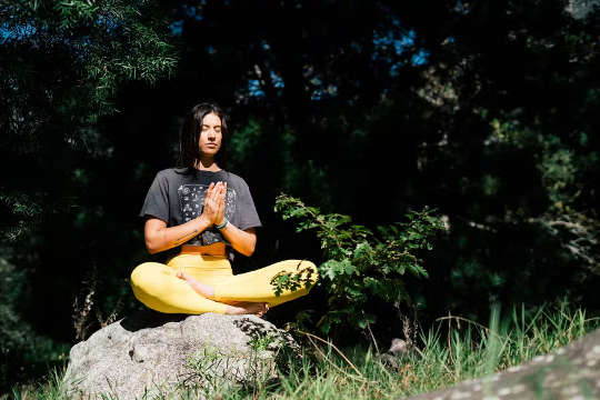 a young woman sitting outside in a lotus position