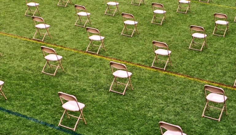 Chairs sit six feet apart on a green field