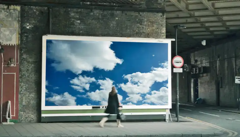 person in grimy underpass walk past billboard image of blue sky with white clouds