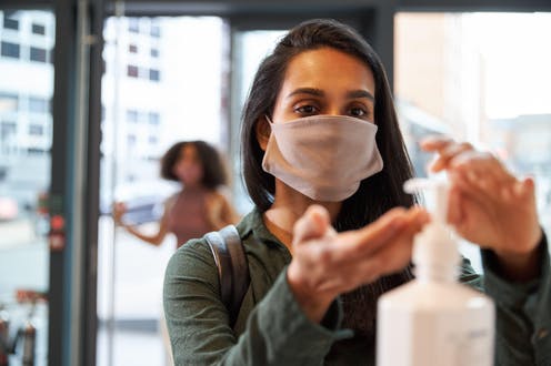 Woman using hand gel as she enters a shop