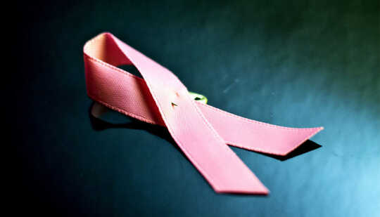 A pink ribbon with a pin in it on a dark blue surface