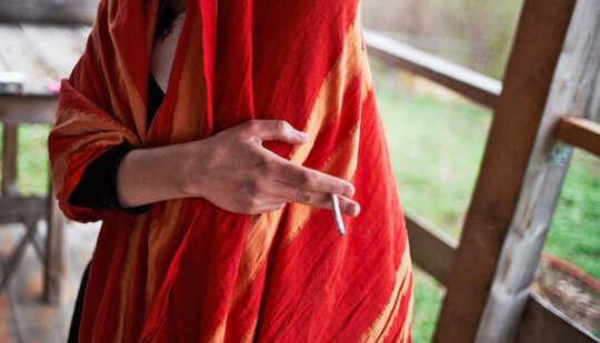 person in red shawl holds cigarette